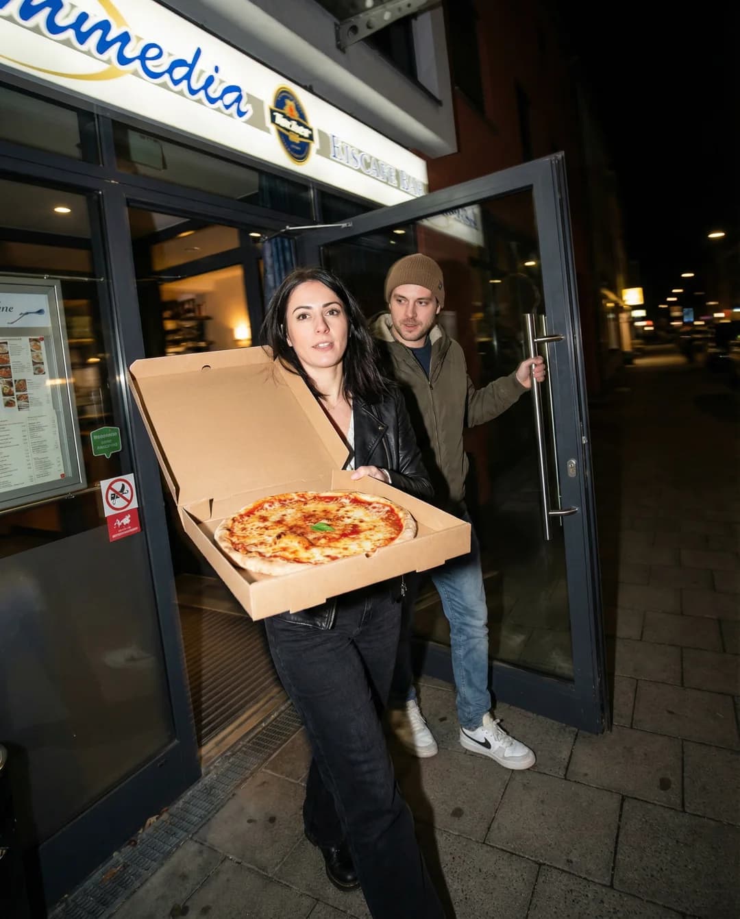 Paar holt nachts eine Pizza vor dem Restaurant ab